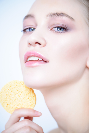 Close-up portrait of a beautiful girl with healthy shiny skin holding a sponge. Beauty, fashion. Skincare, healthcare. Spa for women.の写真素材
