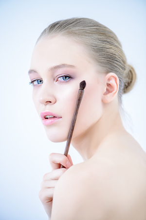 Close-up portrait of a beautiful young woman applying makeup brush. Beauty, cosmetics makeup.の写真素材