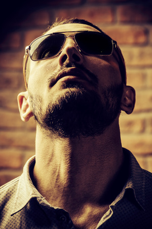 Close-up portrait of a handsome brunet man in sunglasses over brick wall background. Men's beauty, fashion. Men's barbershop, Hairstyle.の写真素材