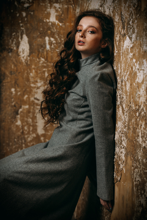 Modern  fifteen-year-old girl with long curly red hair posing over grunge background. Beauty, fashion.の写真素材