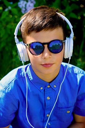 Portrait of a cool boy listening to music with headphones in a summer park. Sunny day.の写真素材