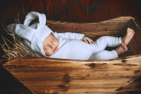 Cute newborn baby lying in a wooden trolley, dressed in rabbit costume. Easter holiday. Scenery in the rustic style.の写真素材