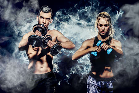 Couple of muscular young people doing exercises with dumbbells. Fitness, bodybuilding. Active, healthy lifestyle.の写真素材