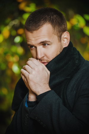 Portrait of a handsome man in classical black coat in the autumn park. Seasonal fashion.の写真素材