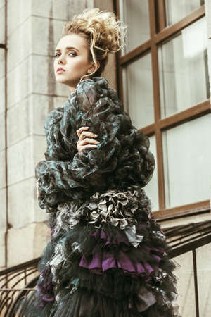 Modern young woman fluffy dress and jacket posing on street to the outskirts of the city. Beauty, street fashion.の写真素材