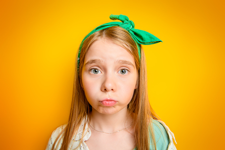 Close-up portrait of a funny emotional girl making faces at camera. Studio shot over yellow background. Childhood concept.の写真素材