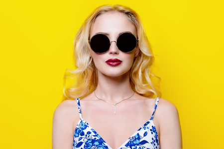 Attractive young woman wearing bright clothes and sunglasses over yellow background.の写真素材