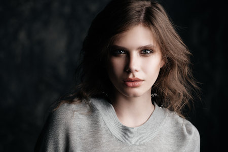 Close-up portrait of a beautiful young woman with natural makeup. Gray background. Beauty, cosmetics, makeup. Hair styling.の写真素材