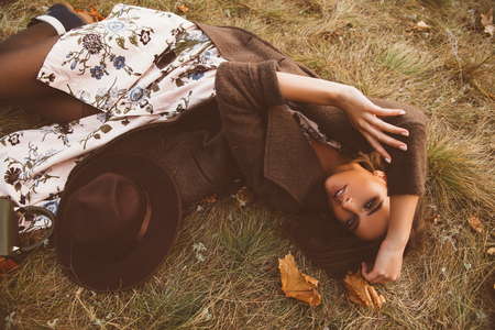 Autumn mood. Beautiful young woman lying on the autumn grass and yellow leaves. Seasonal autumn fashion.の写真素材