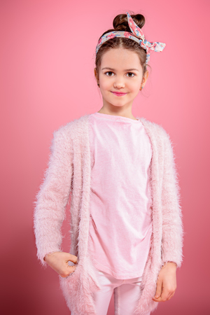 Children's fashion. Cute seven year old girl wearing pink cardigan posing over pink background. Studio shot.の写真素材