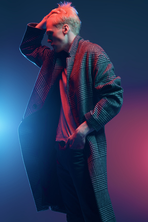 Portrait of a handsome young man with blond hair wearing in a plaid coat, posing at studio over gray background. Men's beauty and health.の写真素材
