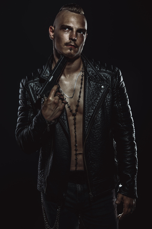 Dark portrait of a serious gangster man with gun wearing black leather jacket.の写真素材