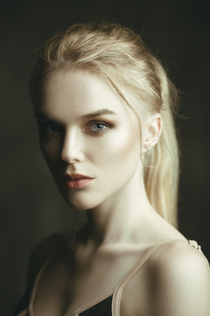 Close-up portrait of a beautiful blonde woman with nude makeup over dark background. Beauty, fashion concept. Make-up and cosmetics.の写真素材