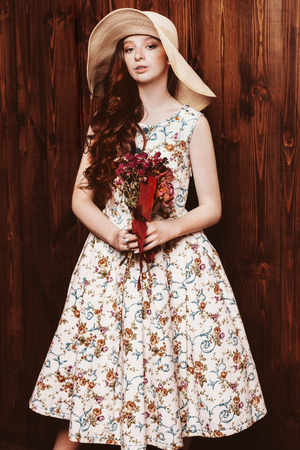 Portrait of a cute girl teenager wearing summer dress and hat by a wooden wall. Beauty, fashion.の写真素材