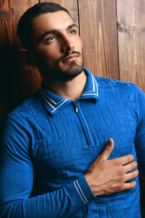Vogue shot of a handsome male model in a T-shirt standing by a wooden wall. Men's beauty, fashion.の写真素材