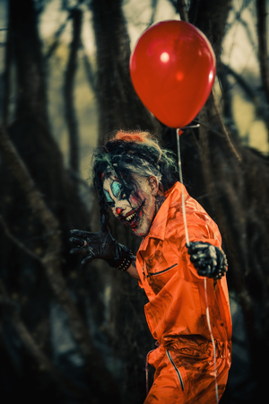 Scary man clown stained in blood in a night forest with a balloon. Male zombie clown. Halloween. Horror.の写真素材