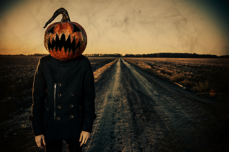 Modern Jack-lantern with a pumpkin on his head stands in a field. Halloween concept.の写真素材