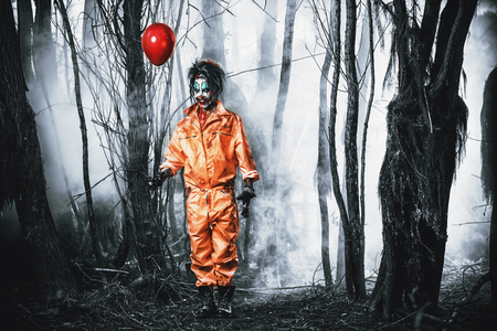Scary man clown stained in blood in a night forest with a balloon. Male zombie clown. Halloween. Horror.の写真素材