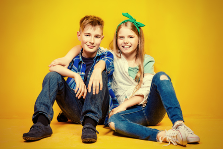Children's fashion. Beautiful  little children sitting at studio over yellow background. Laughing and happy.の写真素材