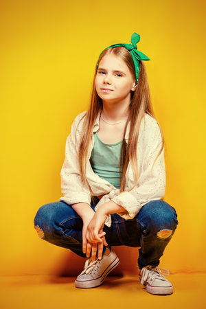 Children's fashion. Beautiful  little girl sitting at studio over yellow background.の写真素材