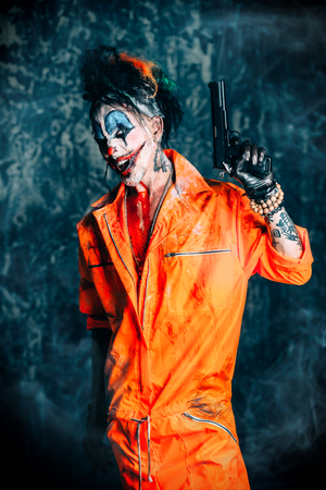 Crazy evil clown man stained in blood is holding a gun. Halloween. Horror, thriller film.の写真素材