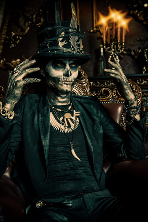 Halloween. A man with a skull makeup dressed in a tail-coat and a top-hat is in the old castle. Baron Saturday. Baron Samedi. Dia de los muertos. Day of The Dead. Old vintage interior.の写真素材