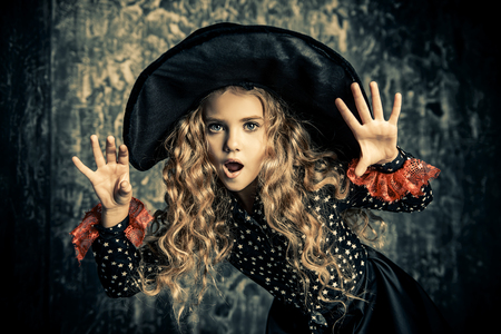 Beautiful child girl in a costume of a witch over grunge background. Halloween party.の写真素材