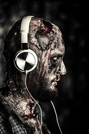 Creepy scary zombie is listening to music with headphines. Halloween. Horror film.の写真素材
