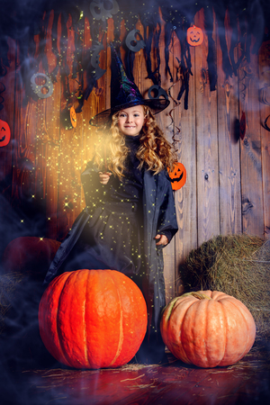 Halloween party. Funny little girl in a witch costume stands near a big pumpkin.の写真素材