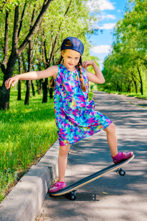 Cheerful little girl riding on a skateboard in the park. Outdoor activity. Summer holidays.の写真素材