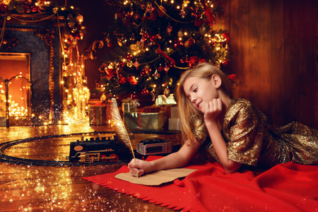 Cute girl near the Christmas tree writing a letter to Santa Claus. Christmas concept. Belief in miracles.の写真素材