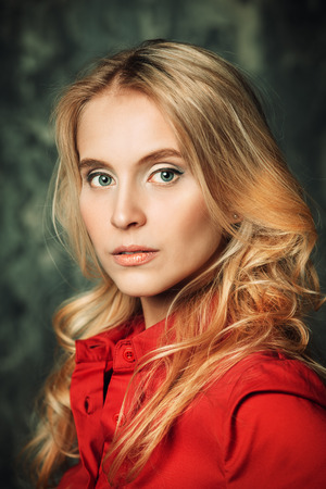 Portrait of a blonde girl in red elegant shirt over grunge background. Beauty, fashion concept. Studio shot.の写真素材