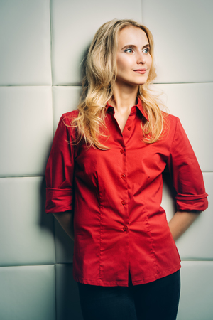 Portrait of a beautiful blonde girl in red elegant shirt over light background. Beauty, fashion concept. Studio shot.の写真素材