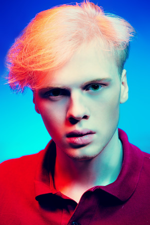 Close-up portrait of a handsome young man with blond hair posing at studio over light background. Men's beauty and health.の写真素材