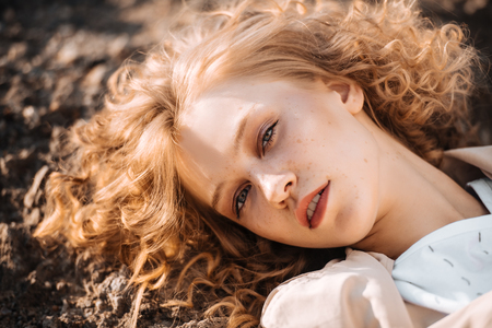 A close-up portrait of a pretty young girl with curlt hair posing outside in nature. Skincare, health, beauty.の写真素材