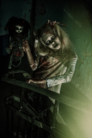 A portrait of scary zombie girl on the stairs with a toy. Halloween. Horror film.の写真素材