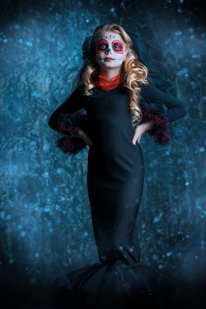 Portrait of a child girl in a costume of Calavera Catrina over dark grunge background. Little girl with sugar skull makeup. Halloween party. Dia de los muertos. Day of The Dead.の写真素材