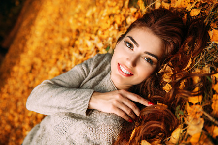 A portrait of a beautiful young woman lying on the ground with golden autumn leaves. Lifestyle, autumn fashion, beauty.の写真素材