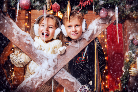 A portrait of children on the porch of their house together. Merry Christmas, happy New Year. Yard with  christmas lights and decorations. Miracle time.の写真素材