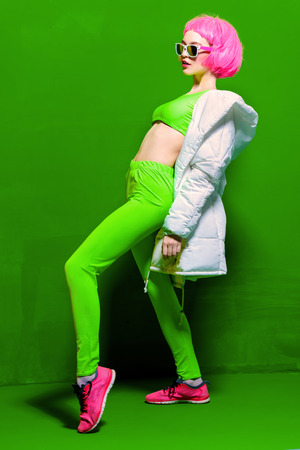 Full length portrait of a trendy girl with pink hair wearing bright stylish clothes. Green background. Beauty, fashion, youth style.の写真素材