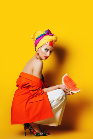 Portrait of a fashionable woman with watermelon and bright make-up. Yellow background. Beauty, fashion, make-up concept.の写真素材