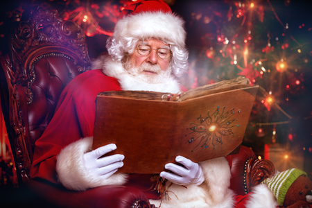 A portrait of Santa Claus sitting at his home with photo album. Miracle time. Christmas, New Year.の写真素材