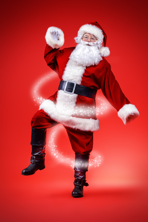 Christmas concept. Portrait of a dancing Santa Claus over red background. Good old traditions. Family holidays.の写真素材