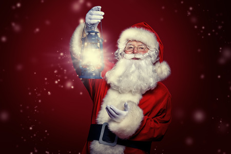 Christmas concept. Portrait of a fairytale Santa Claus is holding lantern over red background. Magic time. Copy space.の写真素材