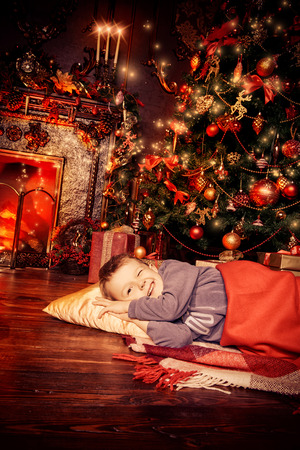 Christmas concept. Cute little boy fell asleep under the Christmas tree waiting for Santa Claus. Time for miracles.の写真素材
