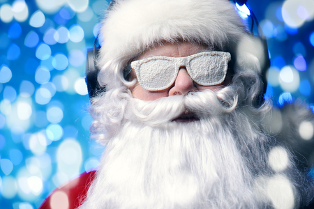 DJ Santa Claus in snowy glasses and headphones. Christmas songs and music. Disco lights in the background.の写真素材