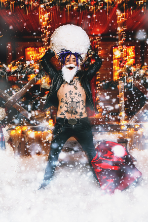 Ð¡heerful punk Santa Claus fools around near his house with a snowball in his hands.の写真素材