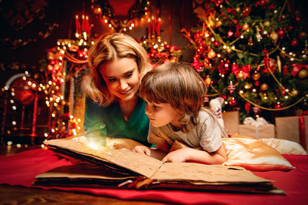 Mother and her son are reading a book at home decorated for Christmas. Family miracle time. Merry Christmas and Happy New Year.の写真素材