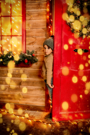 A little boy looking out of the house decorated for Christmas. Miracle time. Merry Christmas and Happy New Year.の写真素材