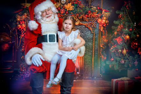 A happy young girl is sitting with Santa Claus at home. Merry Christmas and Happy New Year. Miracle time.の写真素材